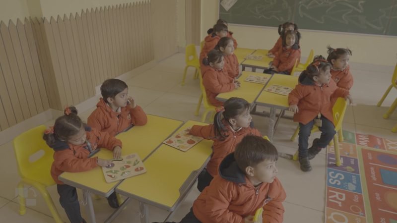 Young children in orange uniforms at a bright pre-primary activity table