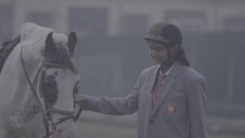 Student in riding helmet leading a white horse
