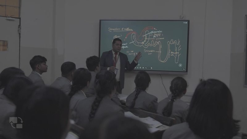 Teacher explaining at a digital board to a full classroom