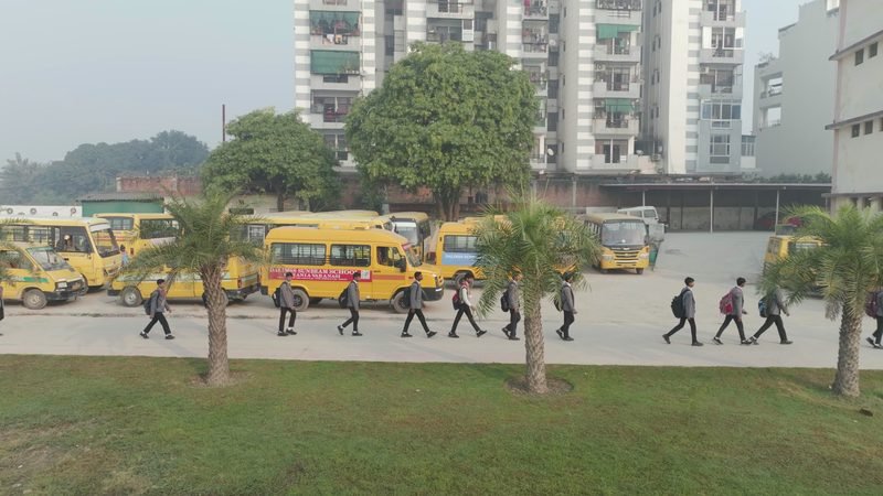 Students walking along the campus road past the school buses, Rohania