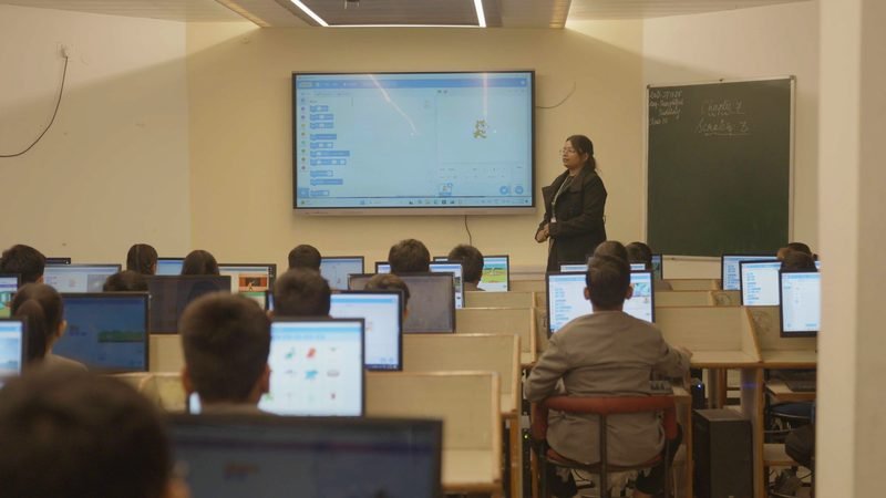 A class in session in the computer lab, with the teacher at the digital board